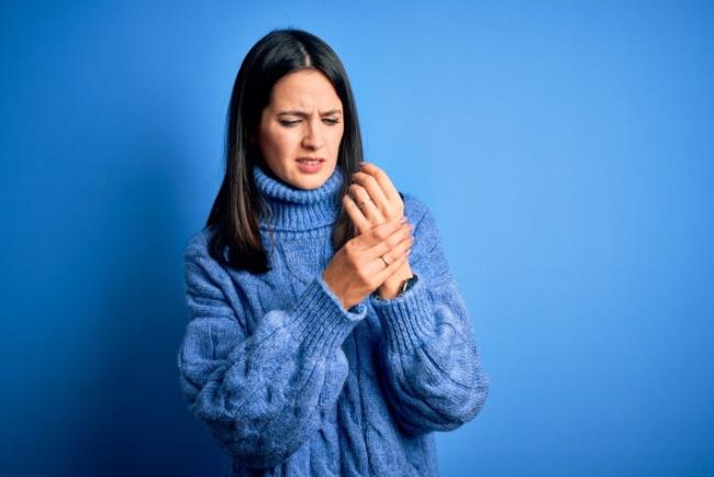 אישה צעירה סובלת מדלקת מפרקים אשר גורמת לכאבים במפרק כף היד בעונת החורף 