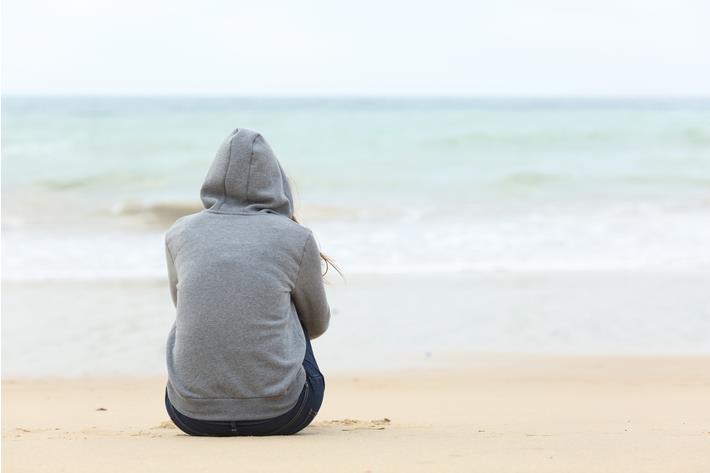 אישה יושבת מדוכדכת על חוף הים, סובלת מדיכאון חורף 