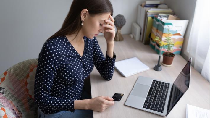 אישה צעירה יושבת עם כרטיס האשראי מול המחשב כדי לבדוק את מצב החשבונות וחווה סטרס כלכלי 